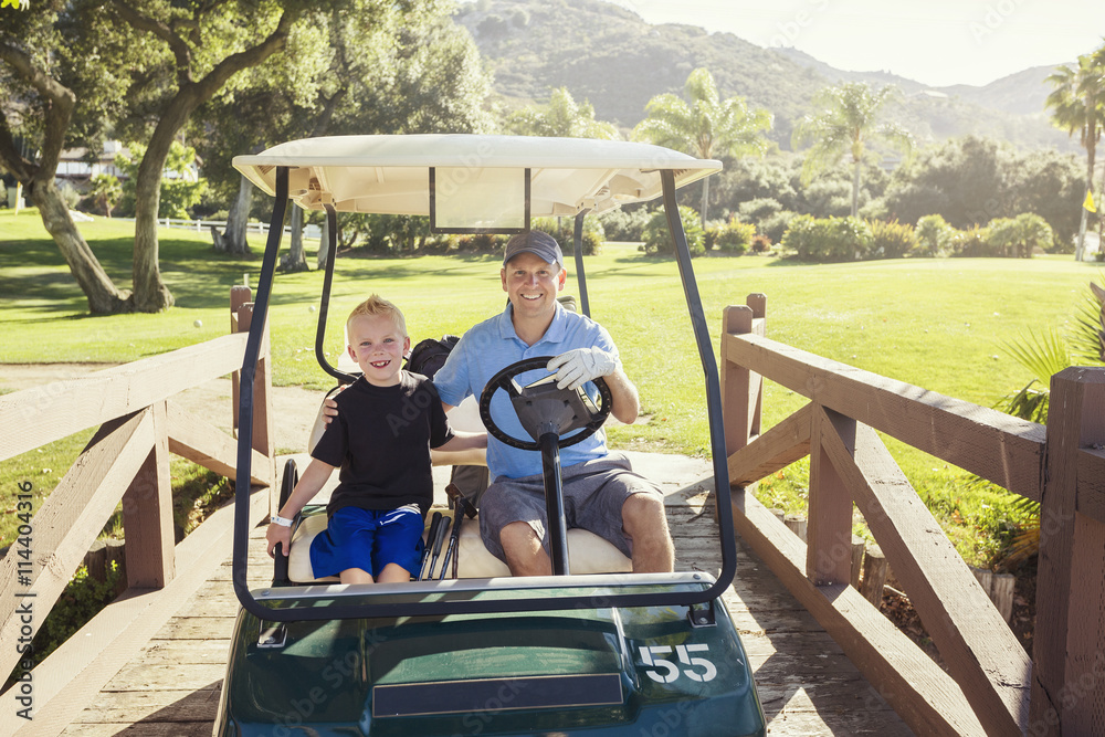 Wall mural father and son golfing together on a summer day riding in a golf cart together