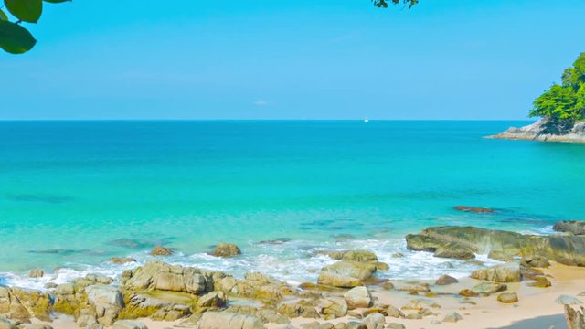 Video 1080p - Azure sky demarks a bold horizon against the deep indigo of the Andaman Sea, with gentle waves lapping at a rocky beach in Kamala, Phuket, Thailand, with sound.