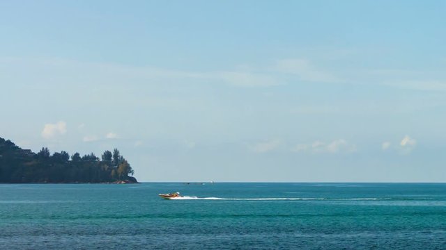 Tourist, flying under a cheerful, rainbow colored parachute, is towed from right to left across the frame in the tropical ocean.