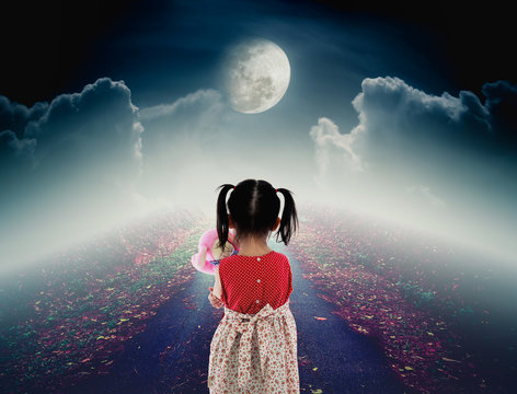 Back view of lonely child with doll sad gesture on pathway with bright full moon.