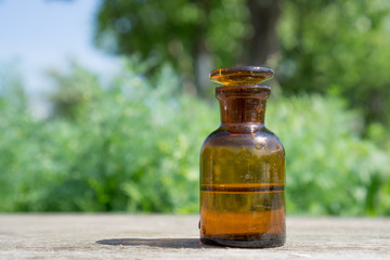 Little brown bottle with water or liquid on wooden board, against the background of vegetation.