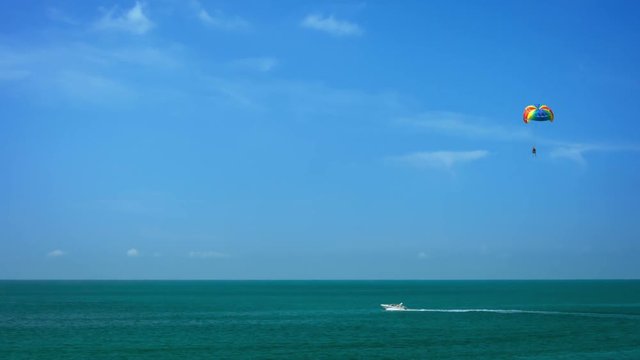 Video 1080p - Parasailing under a rainbow colored parachute, through a bold, blue sky, towed behind a white speedboat on the deep, blue sea.