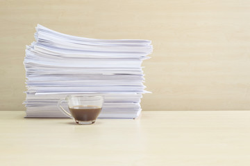 Closeup black coffee in transparent cup of coffee with pile of work paper and calculator on blurred wooden desk and wall textured background in the meeting room under window