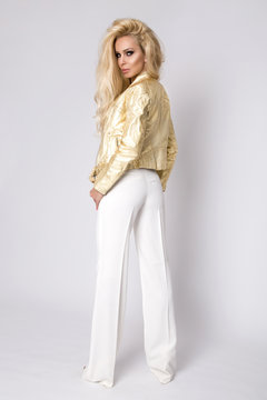 Beautiful sexy blonde woman with long hair standing on a white background dressed in a gold leather jacket biker style on the bike and sensually, tempting looks into the lens