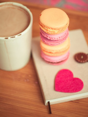 Tasty macaroons, book with cup of coffee staying on wooden table. Good morning. Selective focus.