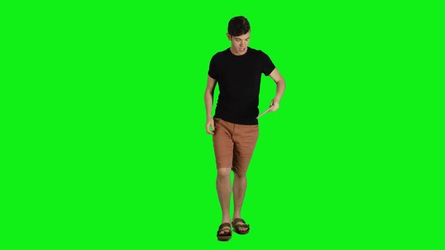 Young man in a full shot walking towards the camera over a green screen. Casual look,  Smiling, taking a selfie, average speed.