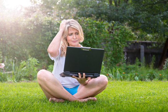 Красивая женщина  на траве в саду с ноутбуком