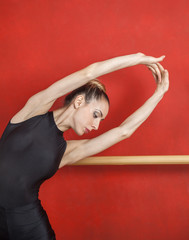 Fototapeta na wymiar Ballerina Stretching With Hands Raised Against Red Wall