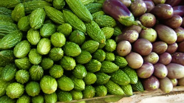 UltraHD video - Big pile of bitter gourds and eggplants on the display table of a vegetable vendor, at a public market in Southeast Asia.