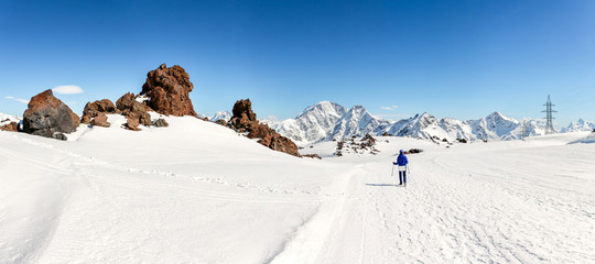 Woman hiking on sunny winter day in mountain landscape. Female hiker in warm bright outfit clothes enjoying trail walk on snow covered track.