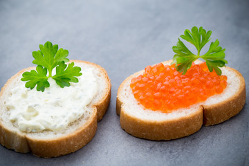 Bread with fresh cream cheese and red caviar on table.