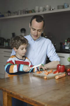 Father looking at son chopping carrot on table at kitchen