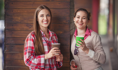 Toned picture of best friends smiling or laughing while holding cups of coffee near cafe or...