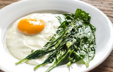Fried egg with spinach on the wooden table