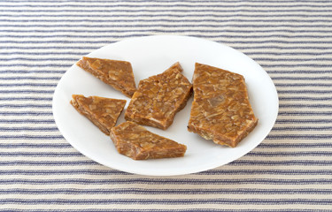 Broken ginger brittle on a plate atop a blue striped tablecloth.