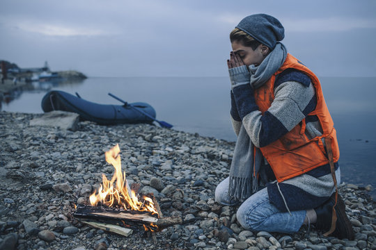 Full length side view of teenage girl sitting by bonfire on lakeshore