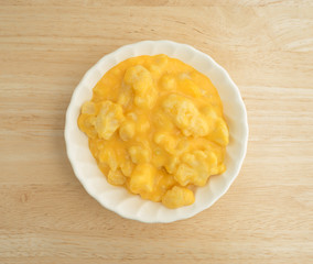 Serving of cauliflower with a cheese sauce in a small bowl on a wood table top view.