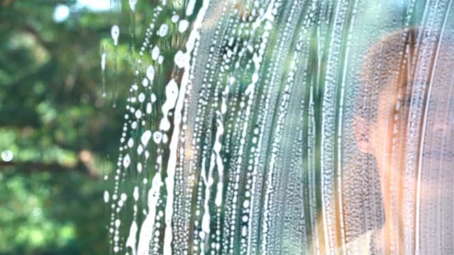 Young attractive woman washes a window using a special brush and a sponge. Dolly shot.