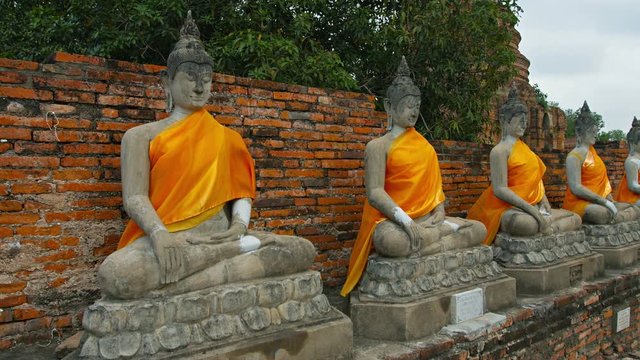Video UltraHD 3840x2160 - Long row of ancient, hand-carved Buddha statues, draped in yellow sashes at Wat Yai Chai Mongkhon, an important temple and monastery in Ayutthay, Thailand.