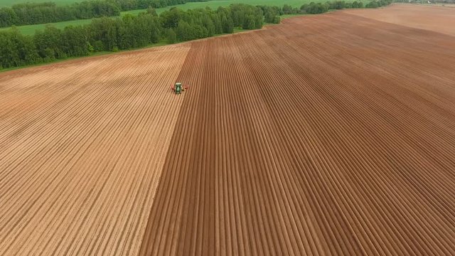 Aerial view of ploughed field with tractor sowing seeds of wheat. Industrial background on agricultural theme.Farm tractor and seeder planting crops on a field.Farm tractor handles field.