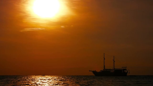 Video 1920x1080 - Tour boat, patterend after an old two-masted pirate ship, riding at anchor just off Patong Beach, Thailand. Silhouetted against a fiery, sunset sky.