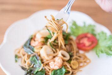 woman eating spicy spaghetti seafood with chicken on wood table.