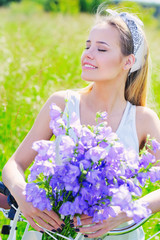 Beautiful young girl with her cruiser bike and flowers in the summer field