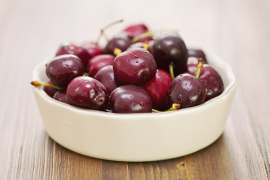 cherries in dish on brown wooden background