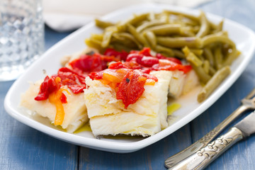 boiled cod fish with red pepper and green beans on white dish and glass of water
