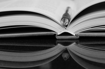 Pen on open book in black and white on shiny marble desk with reflection, close up.