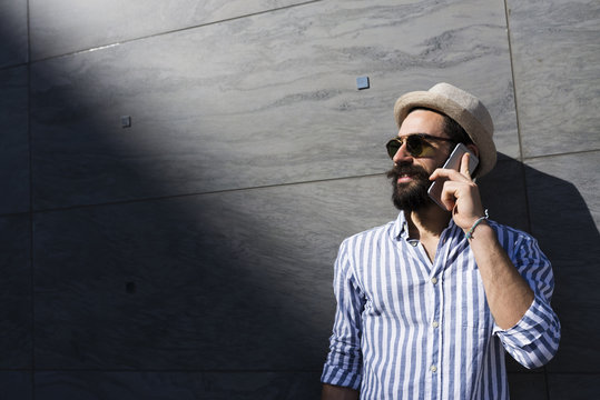 Bearded young man with sunglasses and hat telephoning with smartphone