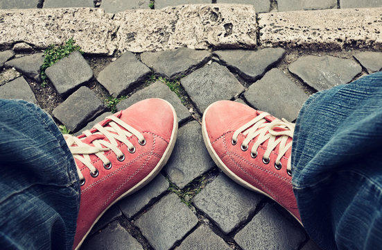 Feet in red sneakers and jeans outdoors.