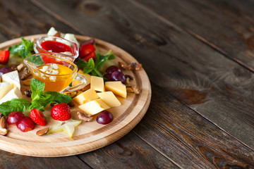 Fruit and cheese plate on wood free space. Top view on round cutting board with different kinds of cheese, fruits and nuts and two sauces. French delicatessen on dark wooden background with copyspace