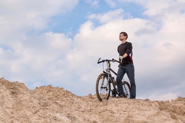 Fototapeta na wymiar Cyclist stands on the sand against the sky