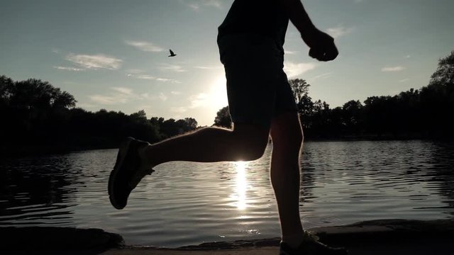 Super slow motion steadicam clip of male runner sunset silhouette against water