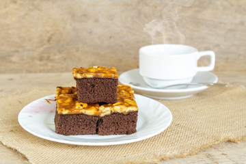 Toffee cake garnish with cashew and hot coffee on wooden table.