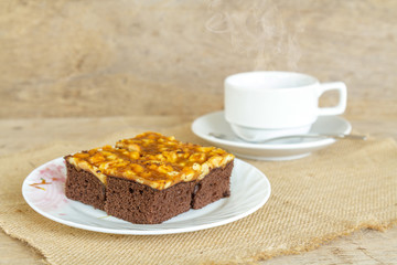 Toffee cake garnish with cashew and hot coffee on wooden table.