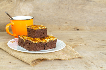 Toffee cake garnish with cashew and hot coffee on wooden table.