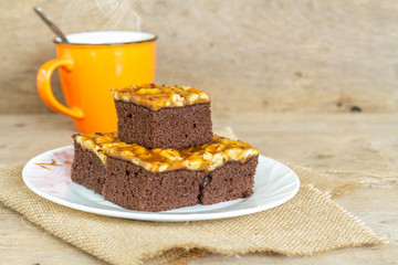 Toffee cake garnish with cashew and hot coffee on wooden table.