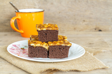 Toffee cake garnish with cashew and hot coffee on wooden table.