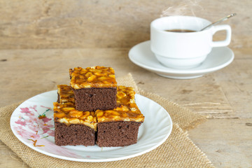 Toffee cake garnish with cashew and hot coffee on wooden table.