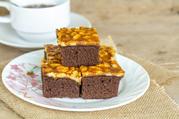 Toffee cake garnish with cashew and hot coffee on wooden table.