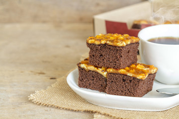 Toffee cake garnish with cashew and hot coffee on wooden table.