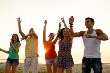 smiling friends dancing on summer beach