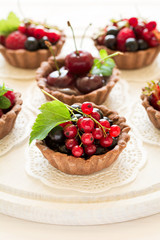Close up of chocolate tartlets with chocolate cream, fresh strawberries, raspberries, blueberries, red currants and cherries on white wooden background. Selective focus