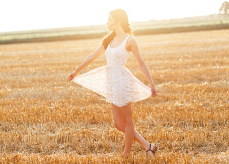 Portrait of beautiful young woman walking through a wheat field at sunset.