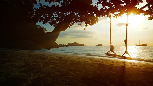 UltraHD video - Small waves gently wash this peaceful, tropical beach in Thailand's Similan Islands, at sunset.  A rope swing hangs from a tree near the water.