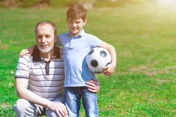 Cheerful old man and his grandchild playing football