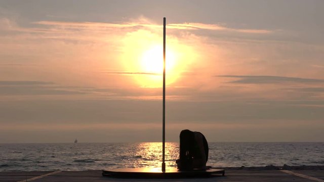 Silhouette of graceful girl dancer during fitness pole dance on the beach in the summer evening at sunset flexible poledancer performing advanced pole tricks and spins against the setting sun part_S1