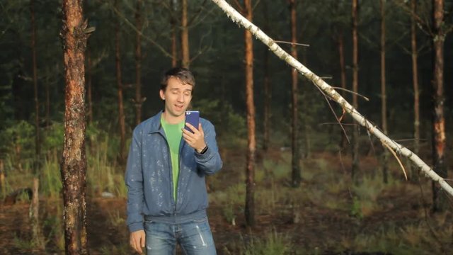 A man makes a video call by phone near a tree in the forest. Early morning